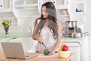 Pretty brunette preparing salad and using laptop