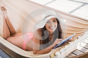 Pretty brunette relaxing on a hammock and using tablet pc