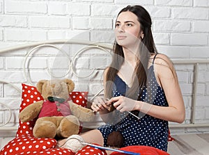 Pretty brunette seamstress engaged in knitting on a bed
