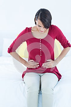 Pretty brunette sitting on bed with stomach pain