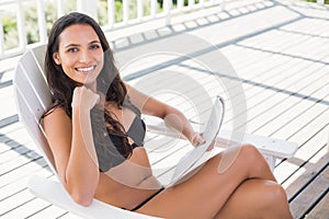 Pretty brunette sitting on a chair and reading magazine