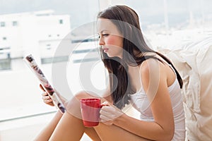 Pretty brunette sitting on floor reading magazine