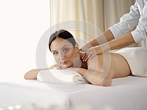 Pretty brunette woman enjoying procedure of back massage in spa salon. Beauty concept