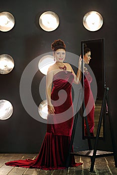 Pretty brunette woman in red long dress poses near