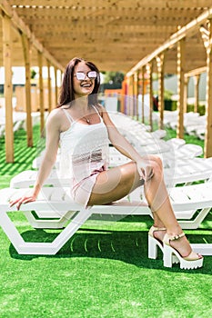 Pretty brunette woman smile relaxing on a lounger outdoors near pool