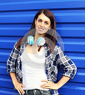 Pretty brunette woman wearing a checkered shirt with headphones over blue