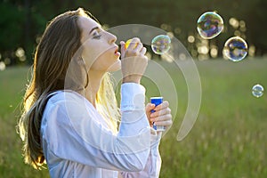 Pretty brunette young woman on a meadow blowing soap bubbles