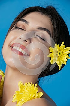 Pretty, brunette young woman standing with yellow flowers, posing, smiling with closed eyes.