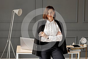 Pretty business lady is wearing a white shirt with a black jacket over her shoulders and black jeans is standing with her arms