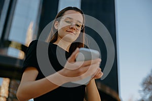 Pretty business woman in eyeglases use mobile phone while standing on modern building background