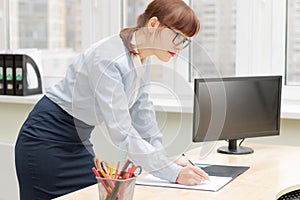 Pretty business woman in glasses in the office at the working table by the window signs documents