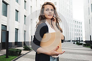 Pretty business woman hold paper documents and discuss financial news on smartphone stand among urban space