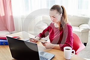 Pretty business woman paying with credit card on smart phone at home office, copy space. Technology, banking, business, online.