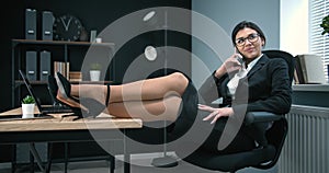 Pretty business woman talking on phone with legs on desk