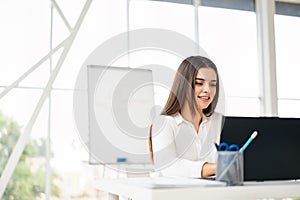 Pretty businesswoman sitting at her desk working on laptop in modern office