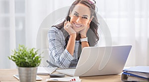 Pretty businesswoman smiles at the camera while sitting at her desk in front of the computer