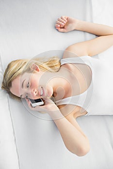 Pretty calm woman lying on her bed while phoning with her smartphone