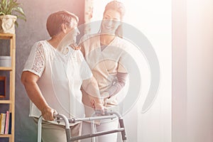 Pretty caregiver and old lady with walker at nursing home