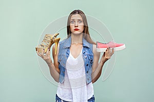 Pretty casual style girl with freckles got choosing sneakers or inconvenient but handsome shoes, and thinking.