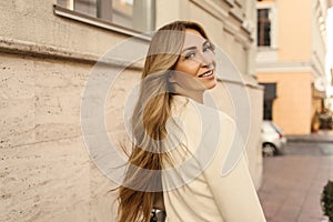 Pretty caucasian adult lady with blond hair looks over her shoulder while walking down street.