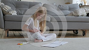 Pretty caucasian blonde artist girl alone draws drawing with colored markers on white album sheet of paper, straightens