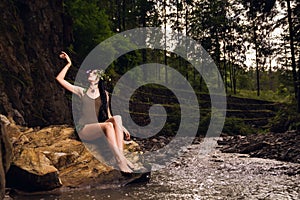 Pretty caucasian female model wearing a flower crown sitting on a rock in the park river