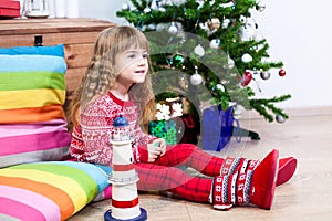 Pretty Caucasian girl sitting on pillows at Christmas eve, red sweater and fur botos