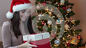 pretty caucasian happy brunette woman Santa hat red gift box decorated fir tree