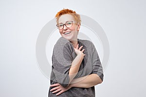 Pretty caucasian mature woman with short red hairstyle in simple pulover is shy to hear a compliment.