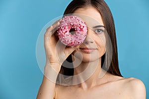 Pretty caucasian model girl hide her eye with pink glaze donuts. Temptation food. Isolated on blue background