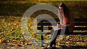 Pretty Caucasian Woman Drinking Coffee and Reading on the Bench in the Autumn Park, Outdoor Relaxation Concept