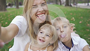 Pretty caucasian woman and her two kids looking at camera smiling. Woman taking selfie with kids. Little boy, girl and