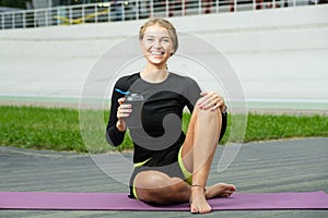 Pretty caucasian woman holding bottle of water in hand and sitting on a purple fitness rug