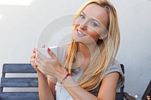 A pretty caucasian woman at home sitting on the porch and drinking coffee