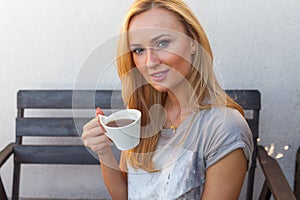 A pretty caucasian woman at home sitting on the porch and drinking coffee