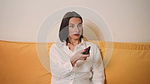 Pretty Caucasian woman watching TV sitting on the sofa couch in living room at home.