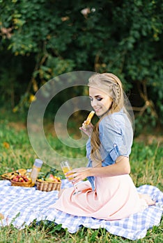 Pretty caucasian young woman with long hair is lsitting on a blanket in nature on a sunny summer day. Picnic, rest, relax in the