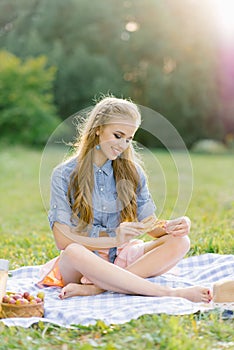 Pretty caucasian young woman with long hair is lying on a blanket in nature on a sunny summer day. Picnic, rest, relax in the