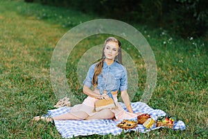 Pretty caucasian young woman with long hair is sitting on a blanket in nature on a sunny summer day. Picnic, rest, relax in the