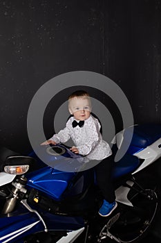 pretty charming little boy on motorcycle on black background. little blonde child riding blue motor bike