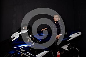 pretty charming little boy on motorcycle on black background. little blonde child riding blue motor bike