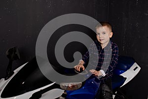 pretty charming little boy on motorcycle on black background. little blonde child riding blue motor bike