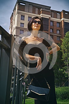 pretty charming middle-aged woman in a black dress, hat and sunglasses strolls through the city park and street