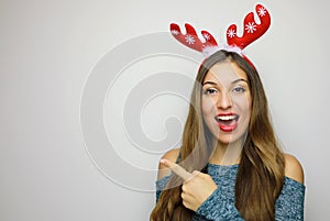 Pretty cheerful christmas woman gesturing with finger and showing away on gray background. Copy space.