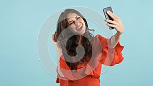 Pretty cheerful girl in red dress happily taking selfie over colorful background