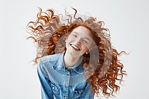 Pretty cheerful redhead girl with flying curly hair smiling laughing looking at camera over white background.