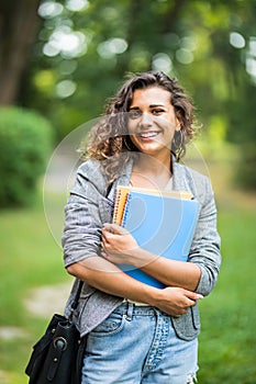 Pretty cheerful student smiling at camera carrying notebook on campus at college