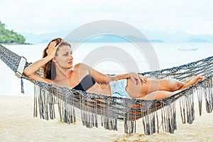Pretty cheerful young girl lying in a hammock on the beach