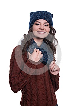 Pretty cheerful young woman wearing knitted sweater, scarf and hat. Isolated on white background. She is smiling.
