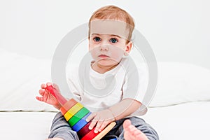 Pretty child 1 years old wearing white tshirt playing with wooden pyramid. Concept of wooden toy, children development